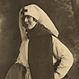 A White female nurse in a scarf, standing and smiling at viewer.