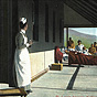 A White female nurse in foreground looking at patients gathered around three cots on a porch.