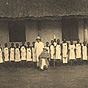 Two White men in pith helmets, in front of line of African female nurses wearing white aprons.