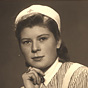 A White female nurse posing for a portrait, right hand to chin, looking at the viewer.
