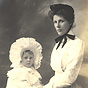 A White female nursemaid in white uniform, standing with a White girl white gown.
