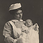 A White female nurse holding a White infant. The nurse looks down at the baby.