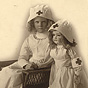 A White girl dressed in a white nursing uniform sits next to a standing nursing doll.