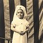 A white girl dressed in a Red Cross nursing uniform, standing before an American flag.