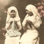 Two White girls dressed as nurses in white, sitting and knitting in a garden.