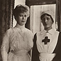 Two White women standing and looking at the viewer, the one on the right is in a Red Cross uniform.