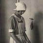 A White female in an apron and head covering at a stove, stirring a pot.