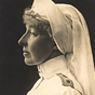 A side profile of a White female nurse (Duchess Hélène), wearing awards and medals on her chest.