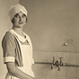 A White female (Princess Astrid)  in an apron and head covering washing bottles at the sink.