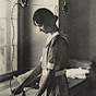 A White female (Princess Astrid) in an apron ironing by a window.