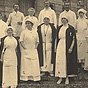 5 White men and 7 White women in medical uniforms, standing on the steps of a building.