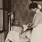 Two White female nurses wearing white aprons, bandage the arm of an elderly White man.