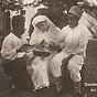 White female nurse bandages the hand of African male soldier, another African soldier assists.