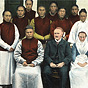 A White doctor and nurse with 10 Asian hospital staff in red, sit for group photograph.