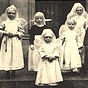 Seven White girls dresses as nun nurses in white and black stand in front of a hospital.