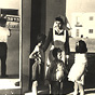A White female nurse in white apron with four White children stand next to a health clinic.
