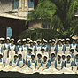 A large group of female nurses in blue and white sit for a group photograph in front of a building.