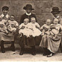 Four White female nurses in long dresses sit with two White babies each on their laps.