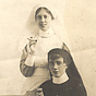 Two White female nurses, one in white the other in black, smoke while sitting for a photo.
