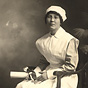 A White female nurse in white, sitting and holding a diploma.