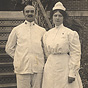 A White female nurse stands with a White male orderly, both in white.