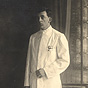 A White male nurse in white, stands in a studio and looks at the viewer.