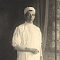 A White male nurse in white, stands in a studio and looks at the viewer.