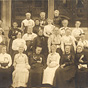 Large group of elderly White women wearing medals sitting and standing in front of a building.