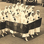 A group of White female Red Cross nurses in white march in a cross formation.