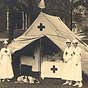 Three White female nurses stand outside a tent, as another woman tends to a man inside the tent.