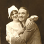 A White man and woman nurse in white, embrace and smile at the viewer.