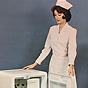 A White female nurse in white looking down at refrigerator she is holding open.