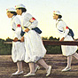 Five Japanese Red Cross female nurses in white carrying a stretcher in a field with building behind.