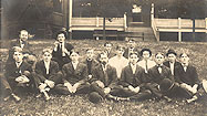 Fifteen White male nurses sitting in a group on a grass lawn.
