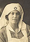 A White female nurse in white apron, leans on a cushion and looks at the viewer.
