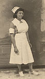 An African American nurse in white stands and looks off to the right.