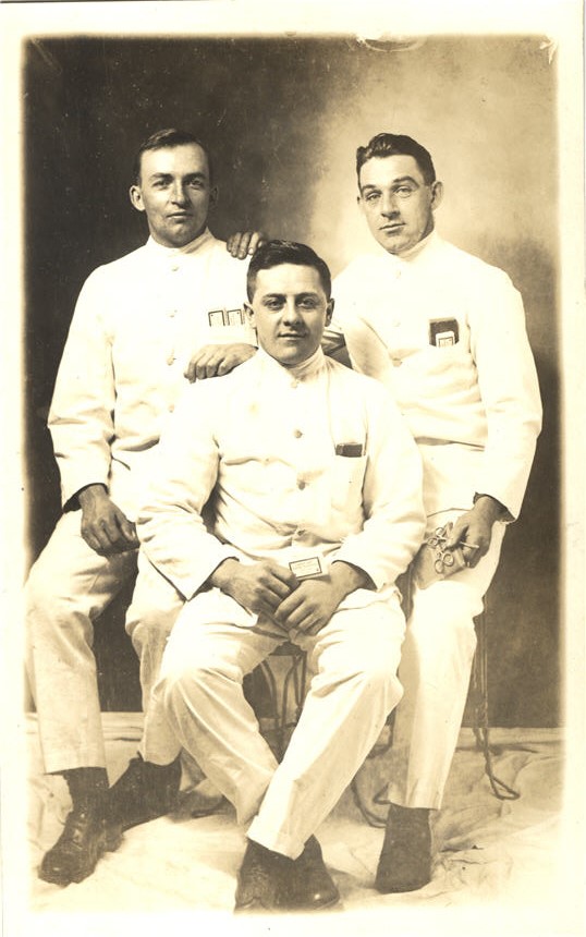 Three White male nurses in white uniform sitting and looking at the viewer.