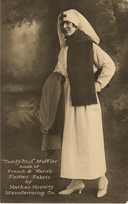 A White female nurse in a scarf, standing and smiling at viewer.