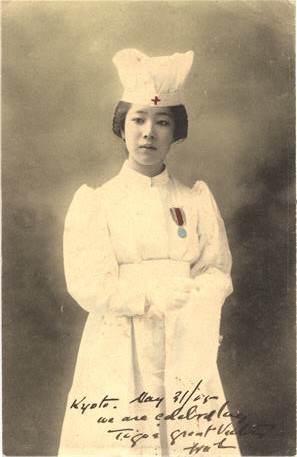 An Asian female nurse in white, wearing war medal, looking slightly off to the left.