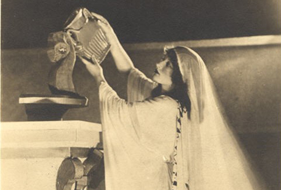 A White female dressed Classically as Hygeia, pouring the contents of a vase on an altar.