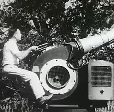 A white man uses a large apparatus to spray pesticide on trees