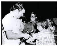 A photograph of a white doctor administering a vaccination to a white girl, as white children look on