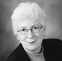 Dr. Barbara Barlow, an elderly White female in a dark jacket and glasses posing for her portrait.