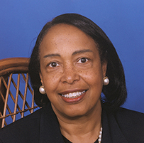 Dr. Patricia E. Bath, an African American female in professional attire posing on a wicker chair with a blue background.