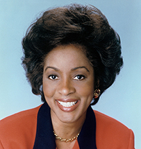 Dr. Lillian M. Beard, an African American female in a red suit with black lapels smiling for her portrait.