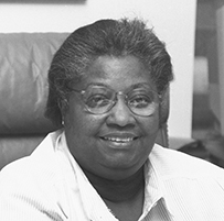Dr. Alexa Irene Canady, a smiling African American female in a collared shirt sitting at a desk chair.