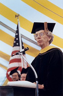 Dr. Jane F. Desforges, a White female in a cap and gown at the podium in front of the American flag.