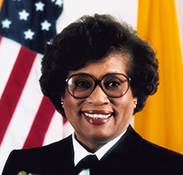 Dr. M. Joycelyn Elders, a smiling African American female in decorated uniform posing in front of the American flag.