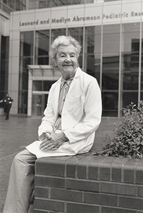 Dr. Audrey Elizabeth Evans, an elderly female in a lab coat sitting outside in front of the building.