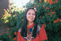 Dr. Bernadette T. Freeland-Hyde, an American Indian female in a red blouse posing outdoors in front flowered shrubbery. 